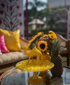 a glass table topped with a yellow plate covered in flowers and animals on top of it