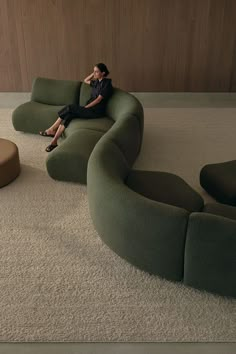 a woman sitting on top of a green couch next to a coffee table and ottoman