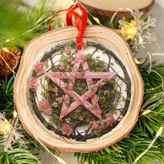 a wooden ornament decorated with pink flowers and greenery, hanging from a christmas tree