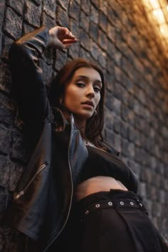 a beautiful young woman leaning against a brick wall