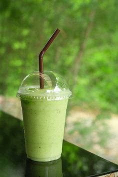 a green smoothie in a plastic cup with a straw sticking out of the top