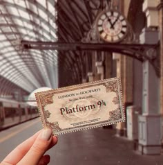 a person holding up a ticket in front of a train station with a clock on the wall