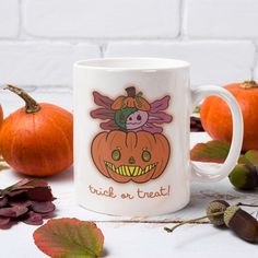 a white coffee mug sitting on top of a table next to pumpkins and leaves