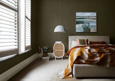 a bed sitting under a window next to a lamp and a painting on the wall