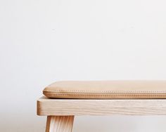 a wooden bench with a tan cushion on it's seat and back rests against a white wall