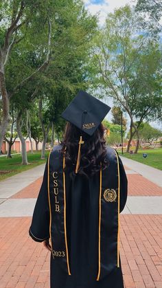 a person wearing a graduation cap and gown walking down a brick walkway with trees in the background