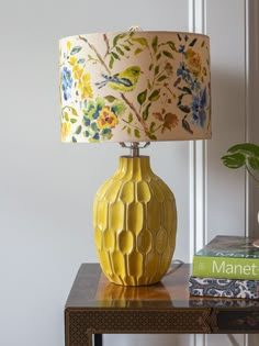 a yellow vase sitting on top of a wooden table next to a book and lamp