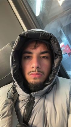 a man with a beard wearing a hooded jacket and looking at the camera while sitting on a bus