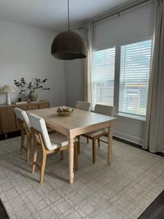 a dining room table with white chairs in front of a window and a rug on the floor