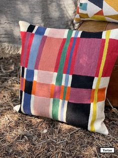 a colorful pillow sitting on the ground next to a wooden bench with grass and mulch