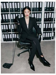 a woman sitting on top of a black chair in front of stacks of binders