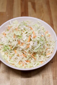 a white bowl filled with coleslaw on top of a wooden table