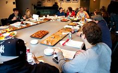 a group of people sitting around a table with food on top of it and papers in front of them