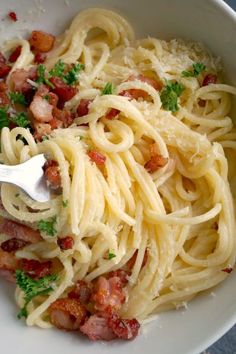 a white bowl filled with pasta covered in bacon and parsley