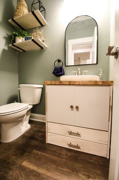 a white toilet sitting next to a bathroom sink under a mirror on top of a wooden counter