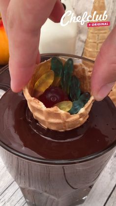 a person placing jelly in a chocolate dessert bowl with leaves and berries on the top