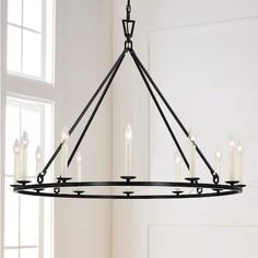 a black chandelier with candles hanging from it's center and two windows in the background