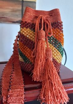 an orange purse sitting on top of a wooden table next to a brown bag with tassels