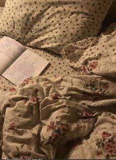 an open book laying on top of a bed next to pillows and sheets with flowers