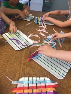 several children are sitting at a table making kites out of strips of colored paper