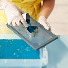 a person in white gloves and yellow shirt is using a spoon to stir something blue