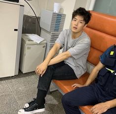 two young men sitting next to each other on a bench in an office building,