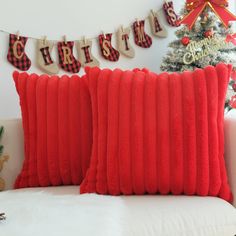 two red pillows sitting on top of a white couch next to a christmas tree and stockings