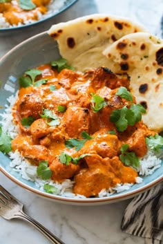 a bowl filled with rice and chicken curry next to pita bread on a marble table