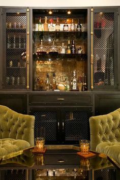 two green velvet chairs sitting in front of a bar with liquor bottles on the shelves