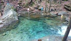 people are standing on the edge of a river with clear blue water, surrounded by rocks and trees