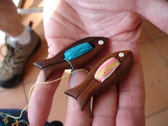 two small wooden birds are being held in someone's hand with yarn on them