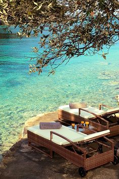 two wicker lounge chairs sitting on top of a beach next to the ocean