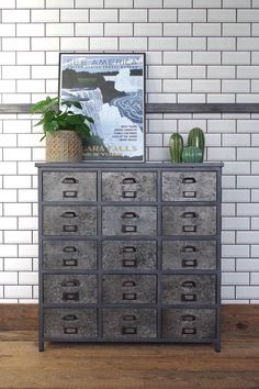 an old dresser with metal drawers in front of a brick wall and potted plant