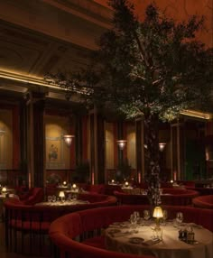 a tree in the middle of a dining room with red chairs and white tablecloths