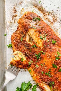 a piece of fish with parsley on the side and a fork in it next to some breadcrumbs