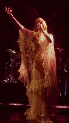 a woman in a long dress on stage with her hands out to the side,