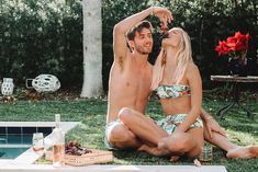 a man and woman sitting next to each other on the grass near a swimming pool