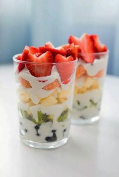 two cups filled with fruit and yogurt on top of a white table next to each other