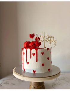 a white cake with red icing and hearts on it, sitting on top of a table