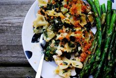 a white plate topped with pasta and asparagus on top of a wooden table