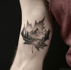 a man's arm with a leaf tattoo on it and mountains in the background