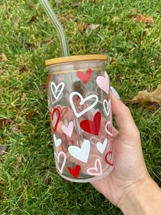 a hand holding a cup with hearts painted on the side and straw in it,