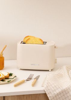 a white toaster sitting on top of a counter next to sliced bread and butter