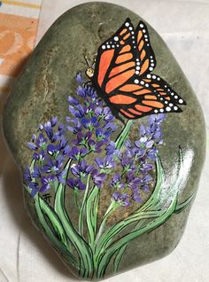 a painted rock with purple flowers and a butterfly on it