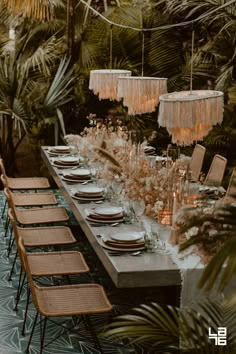 a long table is set with place settings and hanging chandeliers, surrounded by palm trees