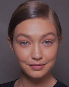 a woman with brown hair and blue eyes posing for the camera in front of a gray background