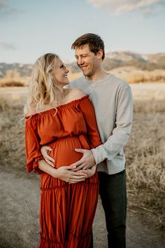 Maternity pictures outside in Bozeman, Montana with mountains in background. Blonde pregnant woman in long rust colored dress smiling and holding belly. Maternity photography couples poses ideas. Maternity Poses For Couples, Maternity Pictures Poses Couple, Maternity Photo Shoot Ideas With Husband, Maternity Couples Poses, Maternity With Husband, Maternity Shoot With Husband, October Maternity Pictures, November Maternity Photoshoot, Bump Poses