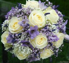 a bouquet of white and purple flowers sitting on top of a glass table next to a fence