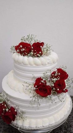 a three tiered white cake with red roses on top