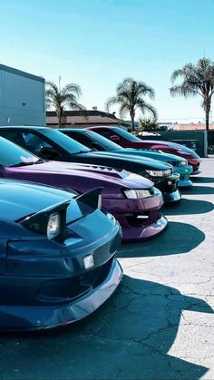 there are many different colored cars parked in the parking lot with palm trees behind them